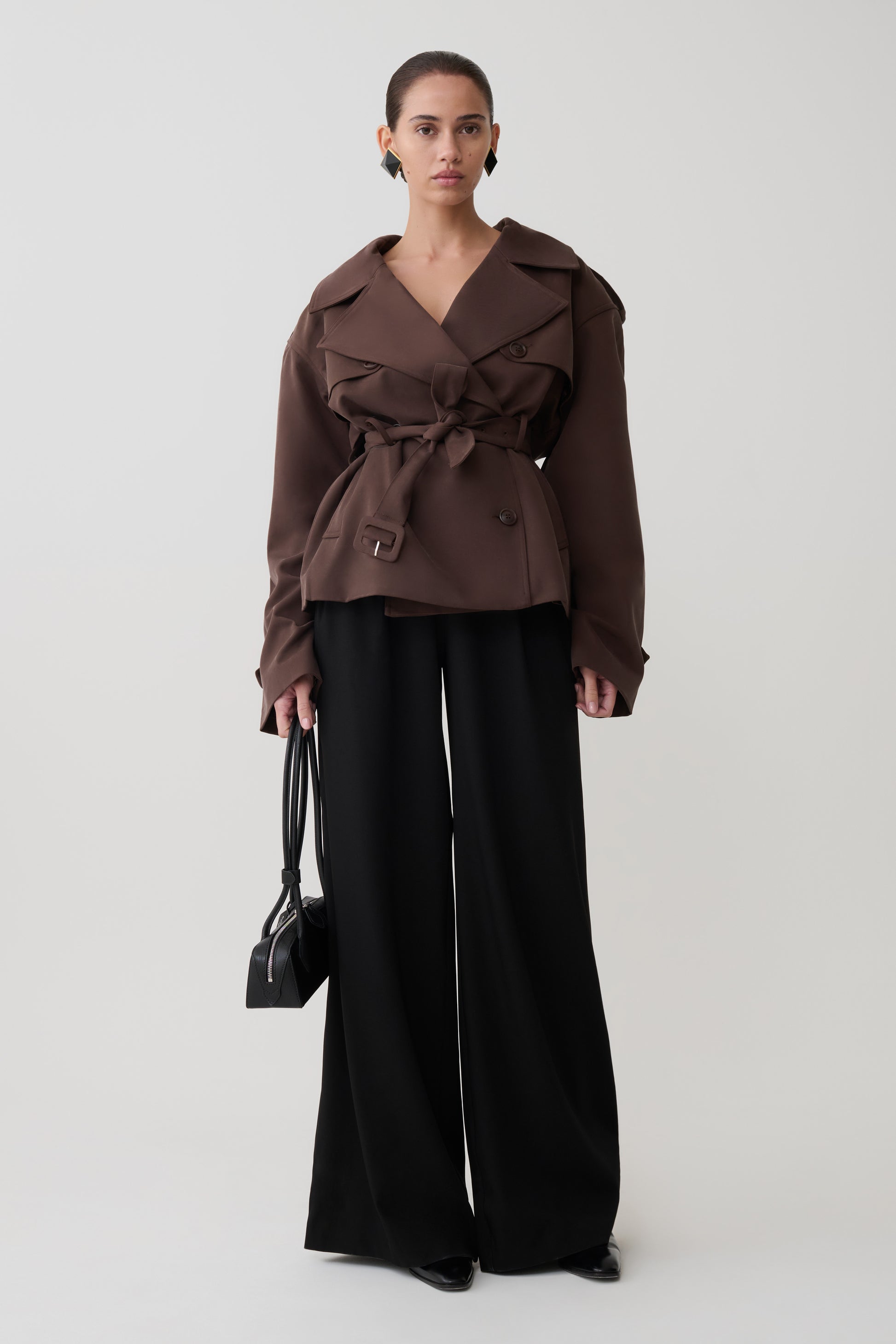 Woman wearing a brown trench coat and black pants on a white background