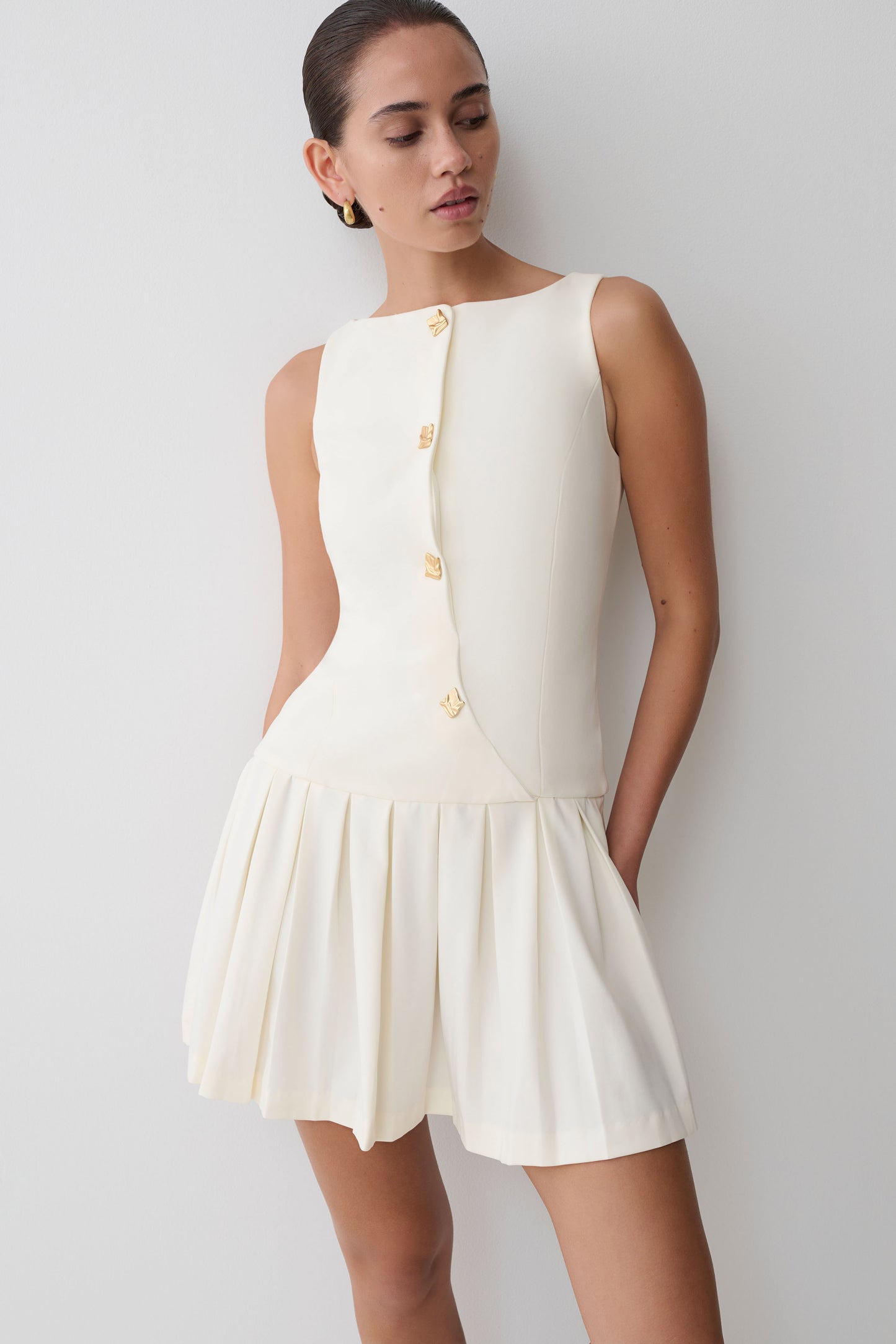 Woman wearing a white dress with buttons against a plain background