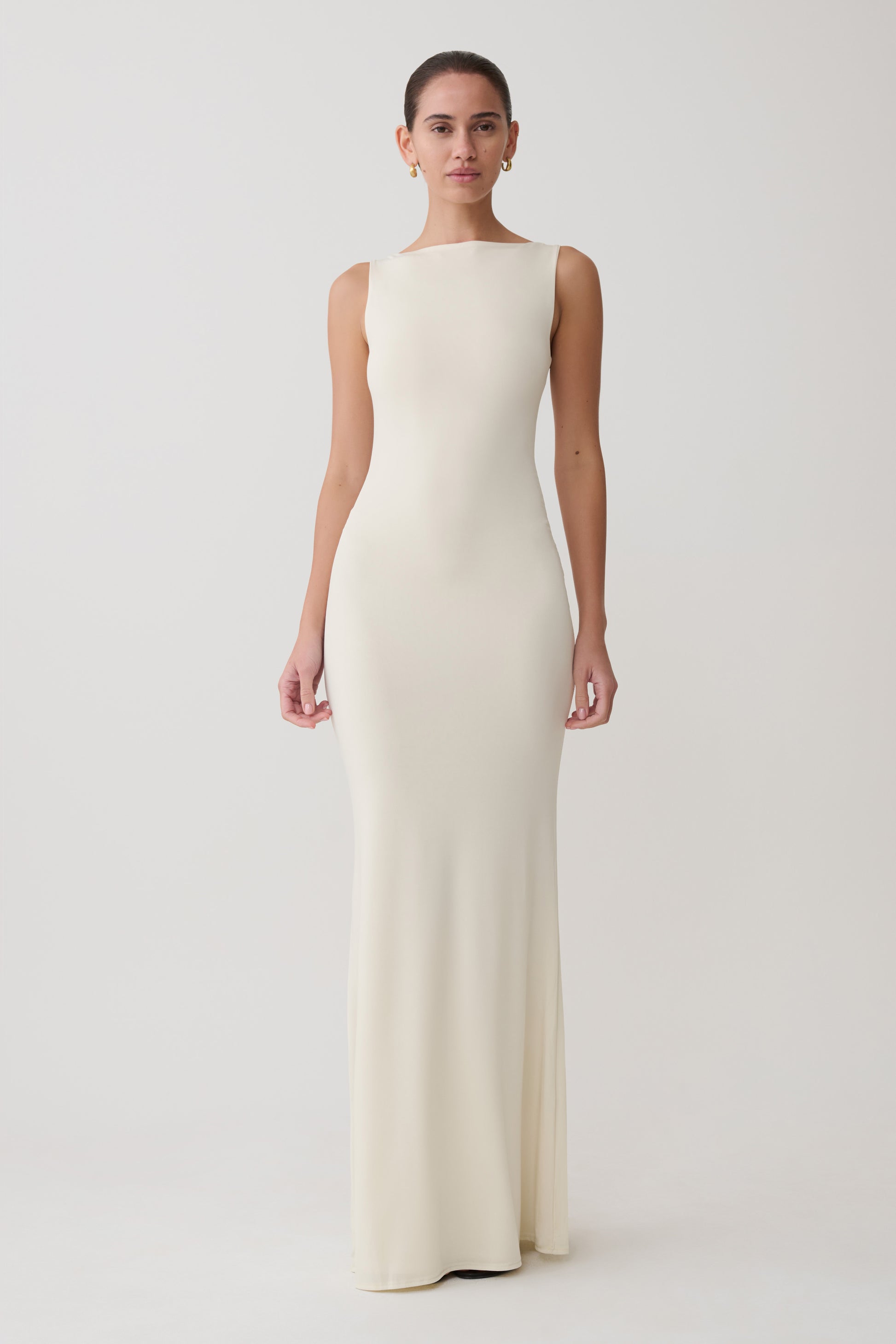Woman wearing a long, off-white dress against a plain background