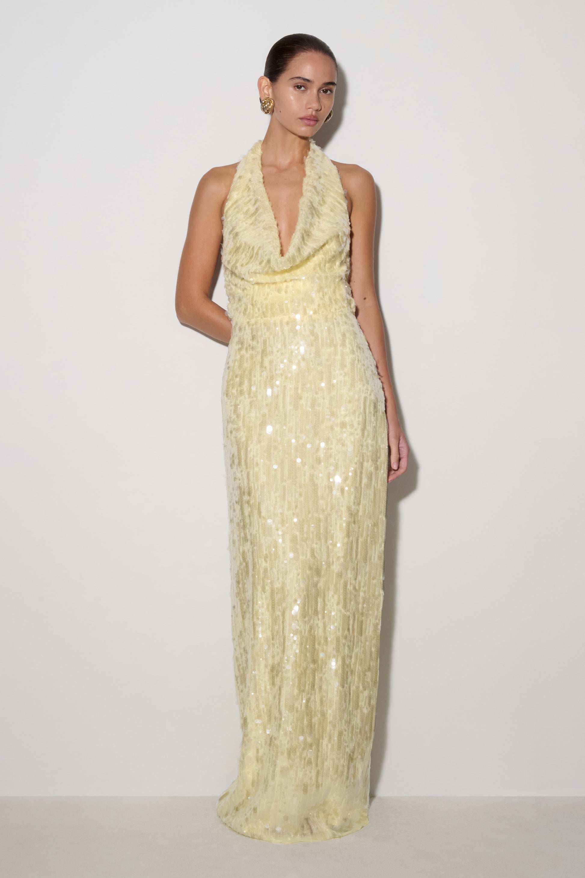 Woman wearing a light yellow sequin gown on a white background