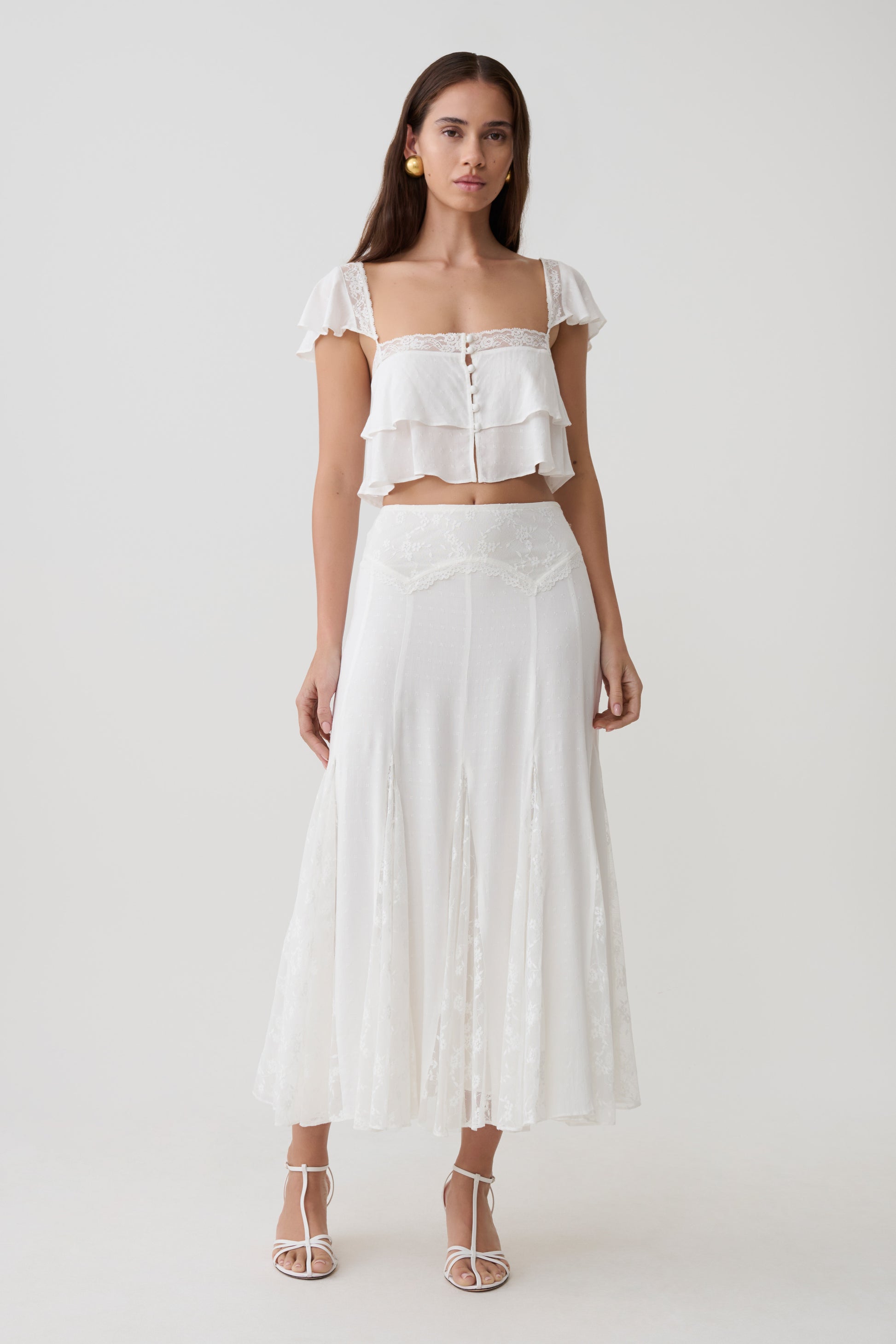 Woman wearing a white lace sleeveless crop top with matching panelled midi skirt.