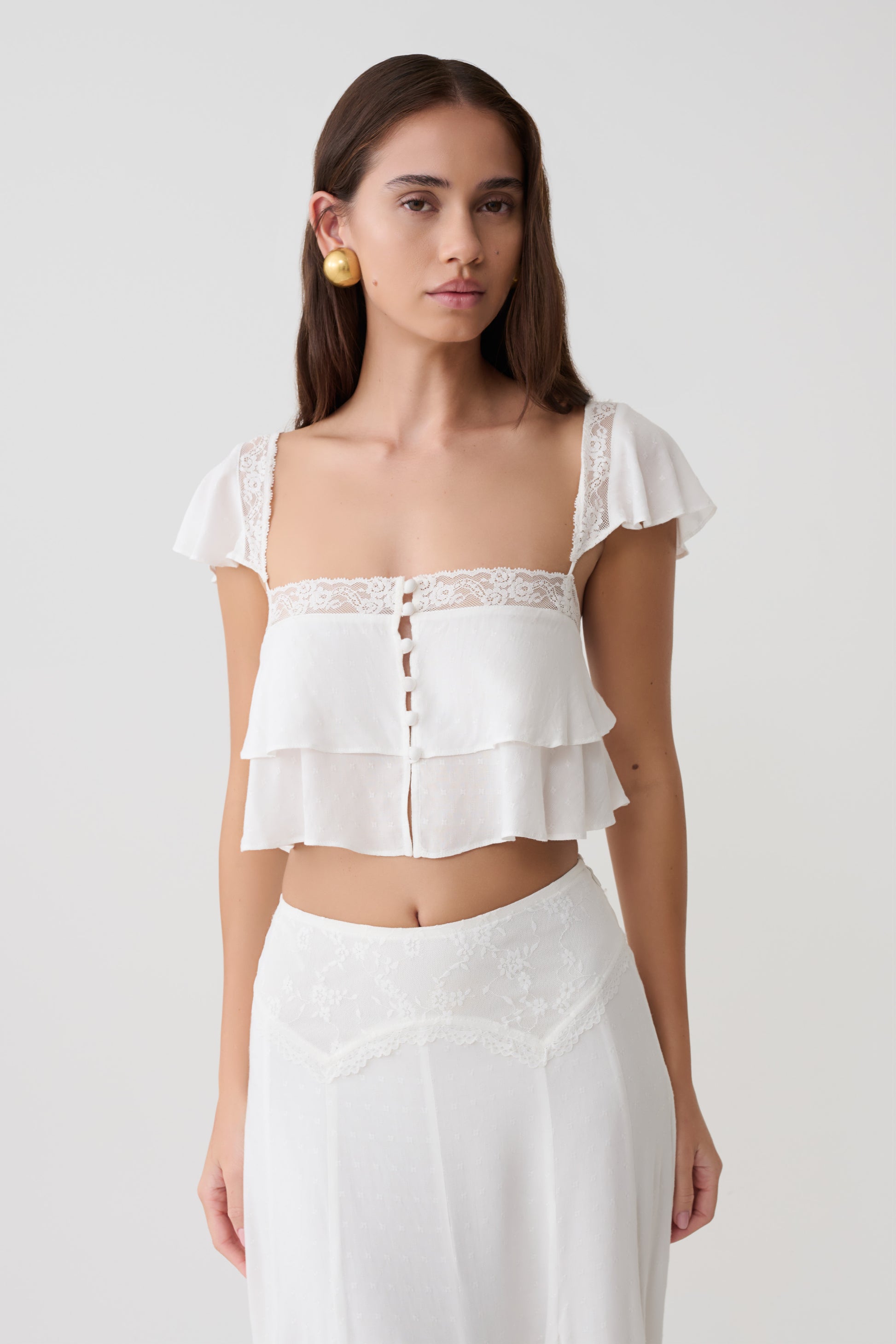 Woman wearing a whie lace sleeveless crop top.