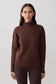Woman wearing a brown ribbed hgih neck sweater.