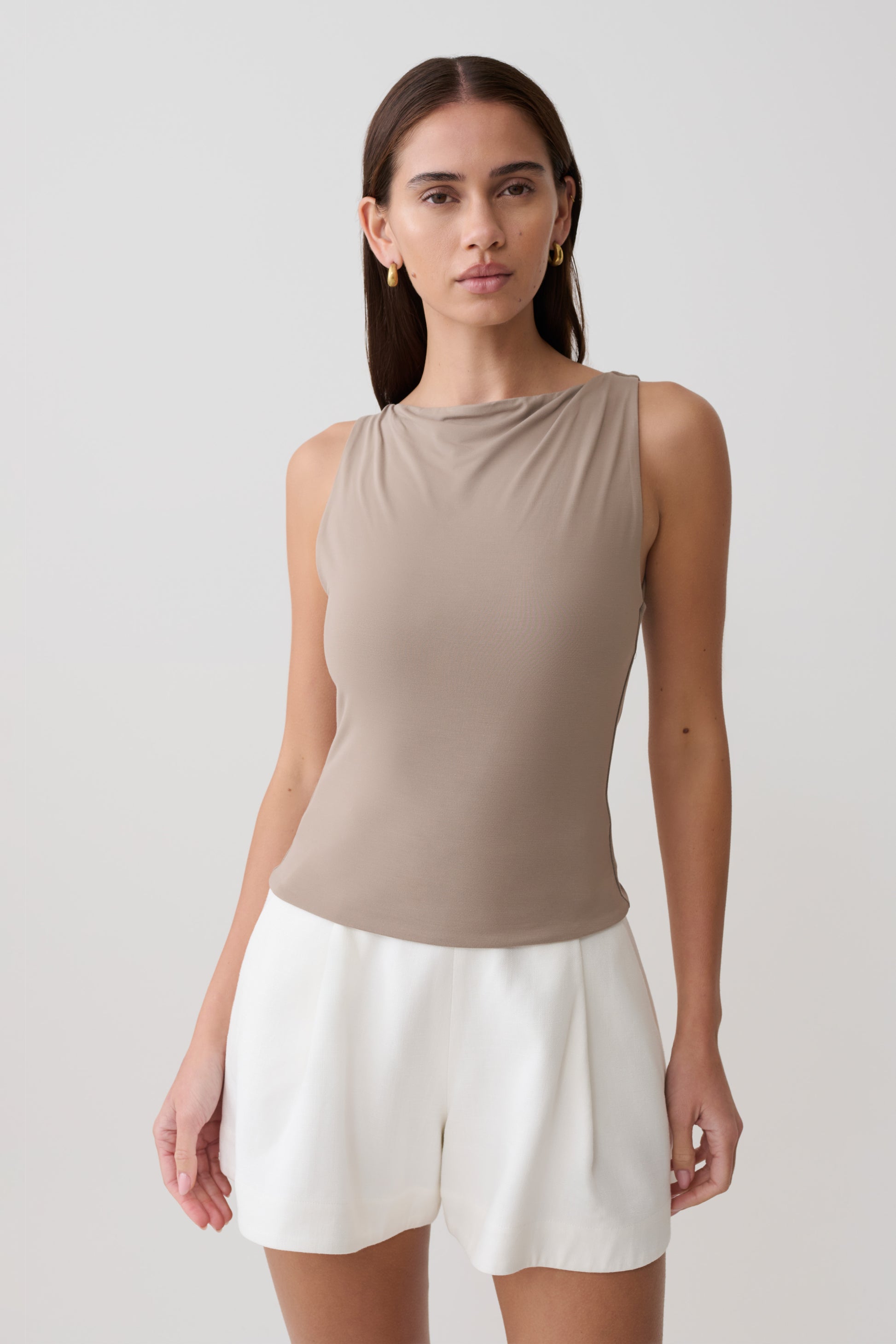 Woman wearing a light brown sleeveless tank top and white shorts.