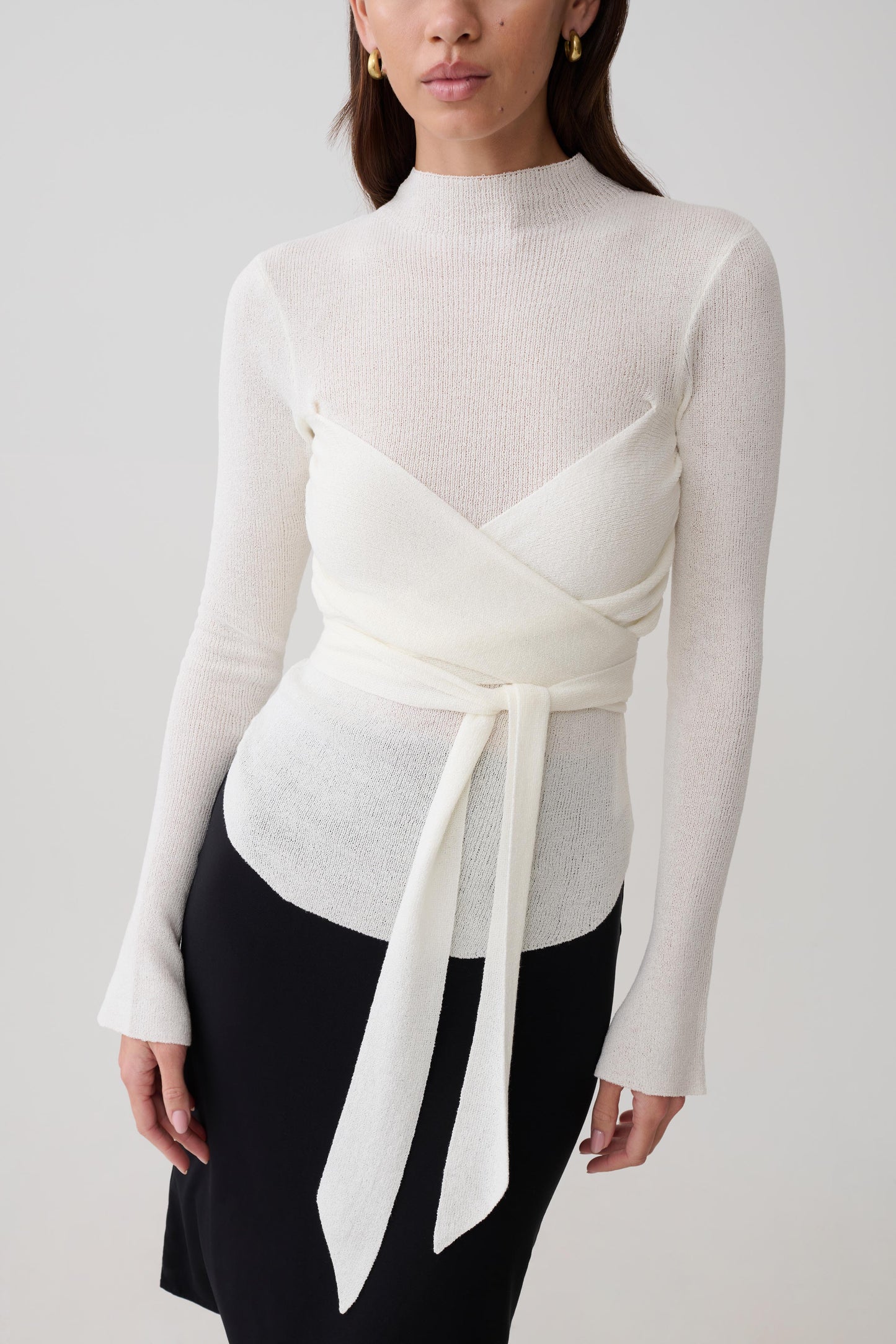 Woman wearing a white knit long-sleeve top with a tie detail.