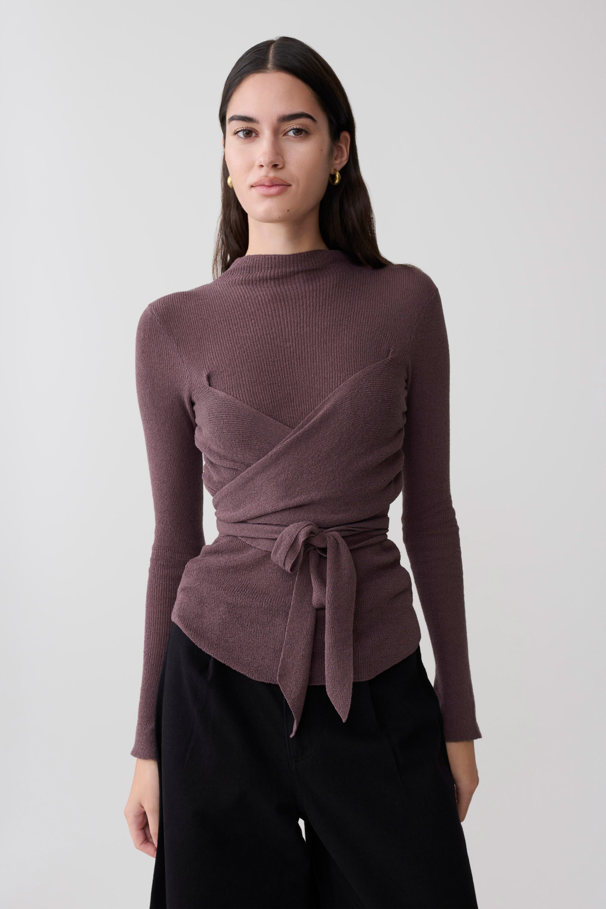 Woman wearing a mauve wrap knit long sleeve top with a tie detail.
