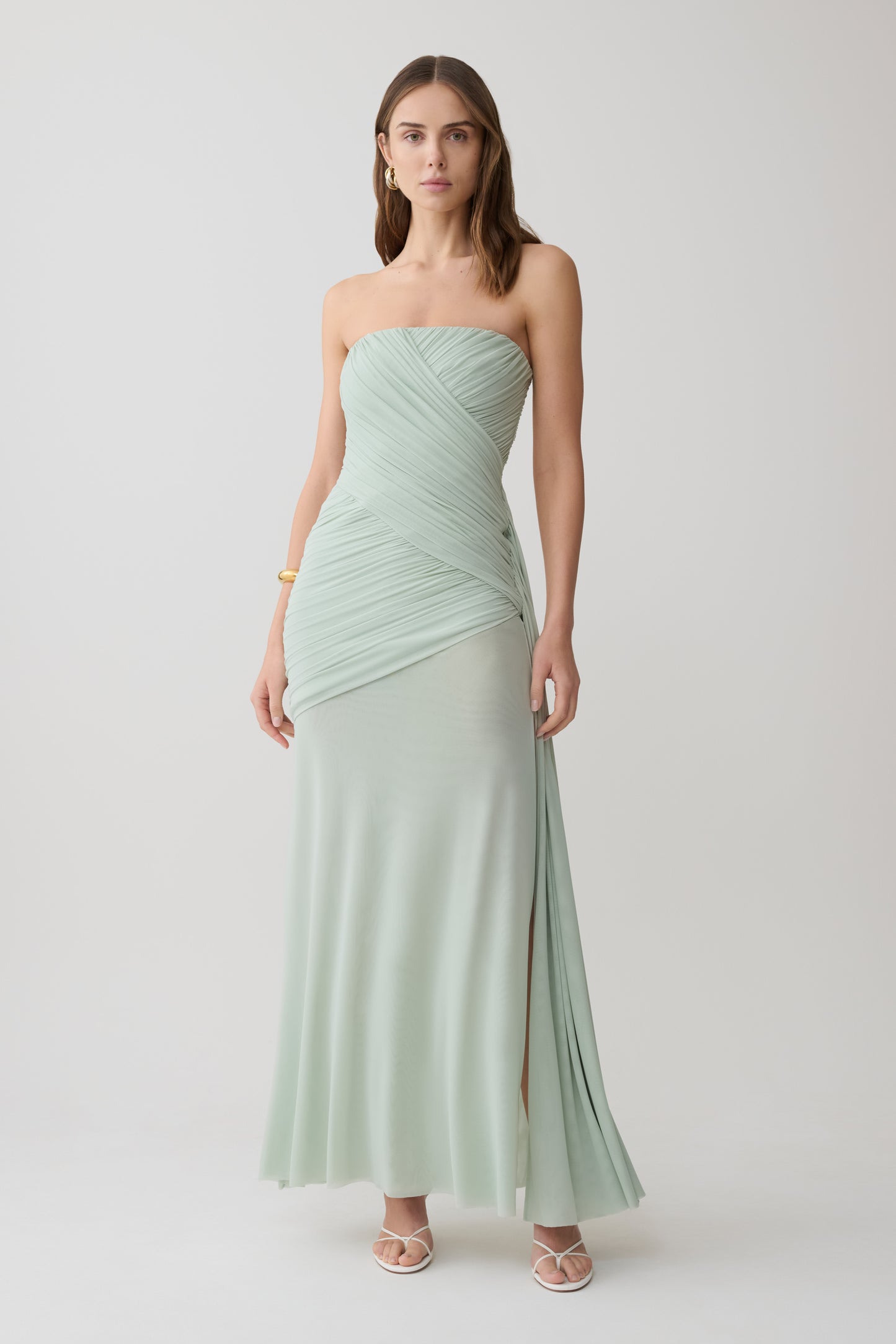 Woman wearing a light green strapless ruched mesh maxi dress.