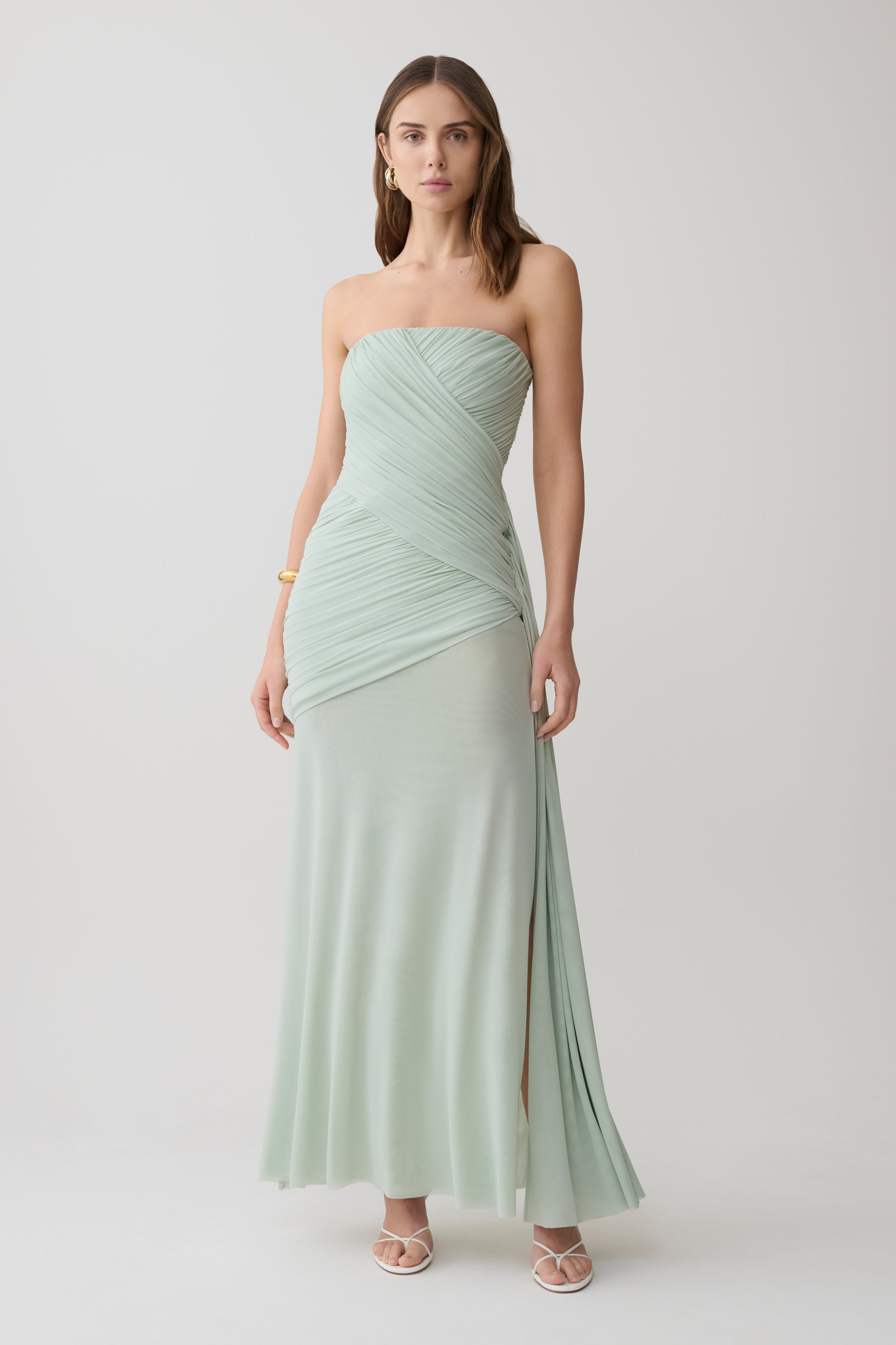 Woman wearing a light green strapless ruched mesh maxi dress.