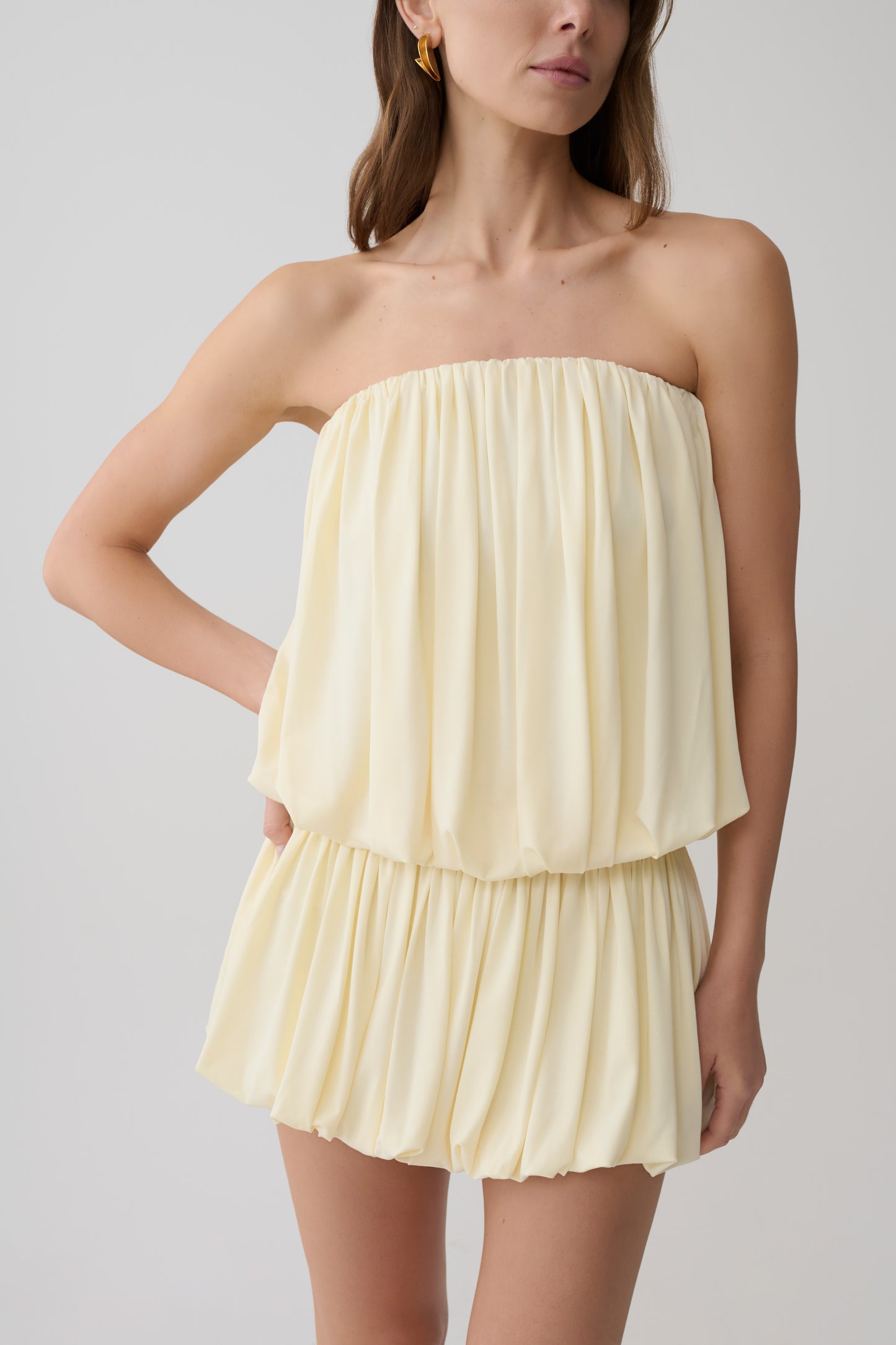 Woman wearing a light yellow strapless gathered bubble mini dress.