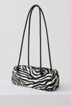 A zebra-print cylindrical shoulder bag with black double shoulder straps, displayed on a clean white studio background.