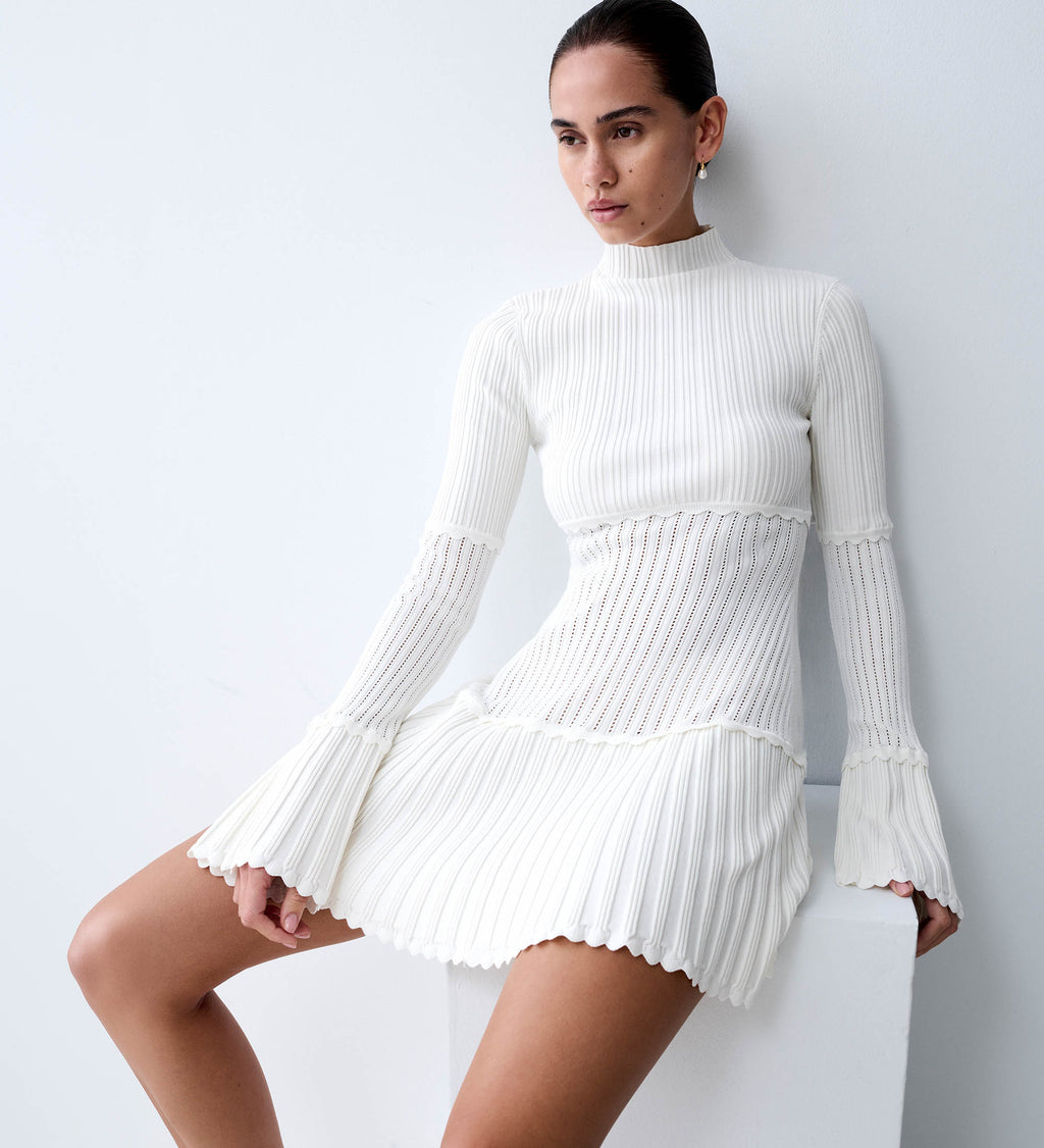 Woman wearing a long sleeve white mini dress.