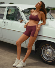 Image of woman leaning on white car wearing a matching maroon and beige activewear set