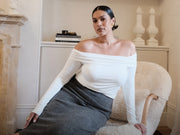 Image of woman in off shoulder white top with charcoal knit skirt.