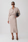 A model wearing a light beige knit long-sleeve collared midi dress, styled with dark sunglasses, a small black handbag, and brown pointed-toe heels against a light gray studio background.