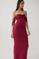 A woman modeling a strapless off-the-shoulder maxi dress in deep burgundy. The dress features a ruched bodice and sheer mesh sleeves, shown against a plain light gray studio background.