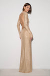 A woman modeling a floor-length champagne beige sequined gown with long sleeves and an open back, photographed against a plain white studio background.