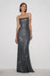 A woman modeling a floor-length, spaghetti-strap evening gown covered in dark gray sequins against a plain light gray studio background.