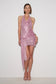 A model wearing a pink sequined halter mini dress with a draped wrap-style skirt and high slit, paired with clear high-heeled sandals, against a plain white studio background.