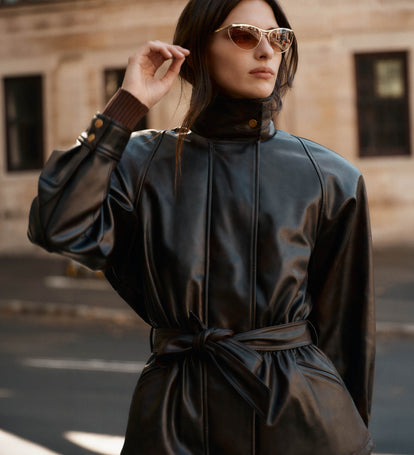 Woman wearing a black leather outfit with sunglasses in an urban setting.