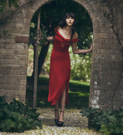 Woman in a red dress standing in a garden with stone arches.