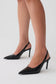 A pair of black pointed-toe slingback high heels worn on a model's feet, shown against a clean light gray studio background.