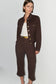 A model wearing a dark brown cropped jacket and matching cropped trousers with gold-tone buttons and a gold belt, styled over a white top against a light gray studio background.