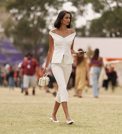 Woman in a white outfit walking outdoors with blurred people in the background.