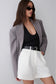A woman modeling a gray blazer over a black top and white shorts with a black belt, photographed against a light gray studio background.