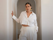 Image of woman in white cropped blouse and suiting pants.