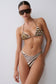 A woman modeling a two-piece bikini with a brown and beige abstract pattern on the top and a brown and white zebra-like stripe pattern on the bottom, paired with dark sunglasses, against a plain light gray background.