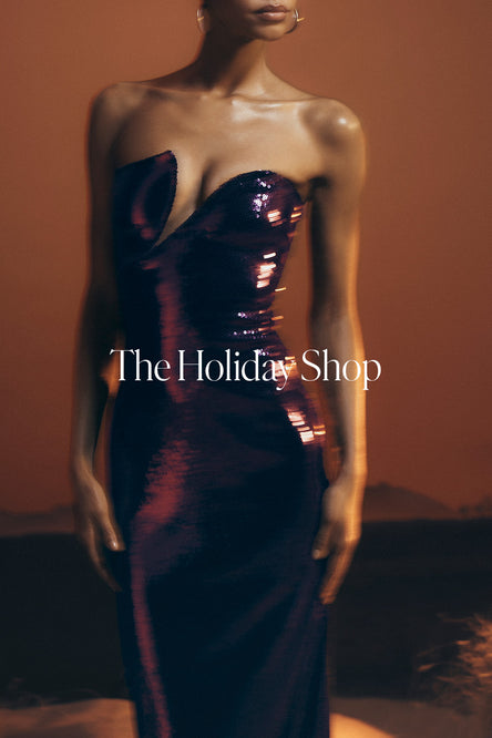 Woman wearing a strapless, shiny purple dress against a warm-toned background with 'The Holiday Shop' text.