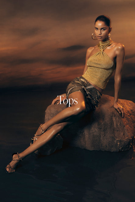 Woman sitting on a rock with a dramatic sky, wearing a gold top and skirt.
