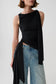 A model wearing a black draped sleeveless top with a side tie detail and light-wash blue jeans, photographed against a light gray studio background.