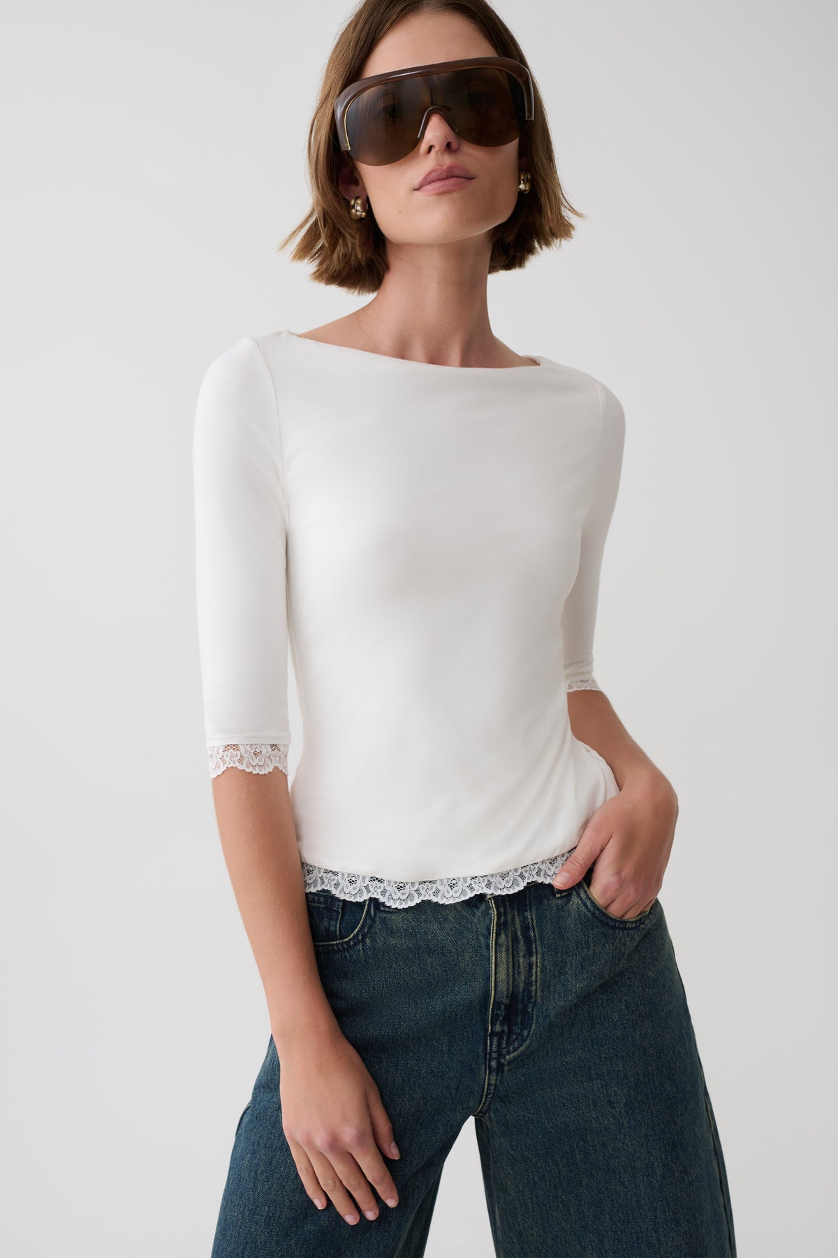 Woman wearing white lace trimmed top, paired with blue jeans and sunglasses.