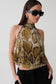 A woman wearing a snakeskin print halter crop top in brown, beige, and black, paired with black pants and black sunglasses, against a light gray studio background.