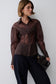 A woman models a sheer, long-sleeved button-up blouse in a dark brown color, paired with dark wide-leg trousers and holding a black textured clutch bag against a plain light gray background.