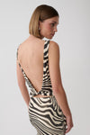A woman shown from the back wearing a zebra-print dress with a deep open back and tie detail, photographed against a light gray studio background.