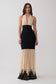 A woman modeling a sleeveless halter-neck maxi dress with a black fitted waist and skirt, and a sheer beige lower skirt with black lace trim at the hem, against a light gray studio background.